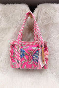 A small pink tote bag with a floral print and pink-and-white striped handles, resting on a white faux fur surface.
