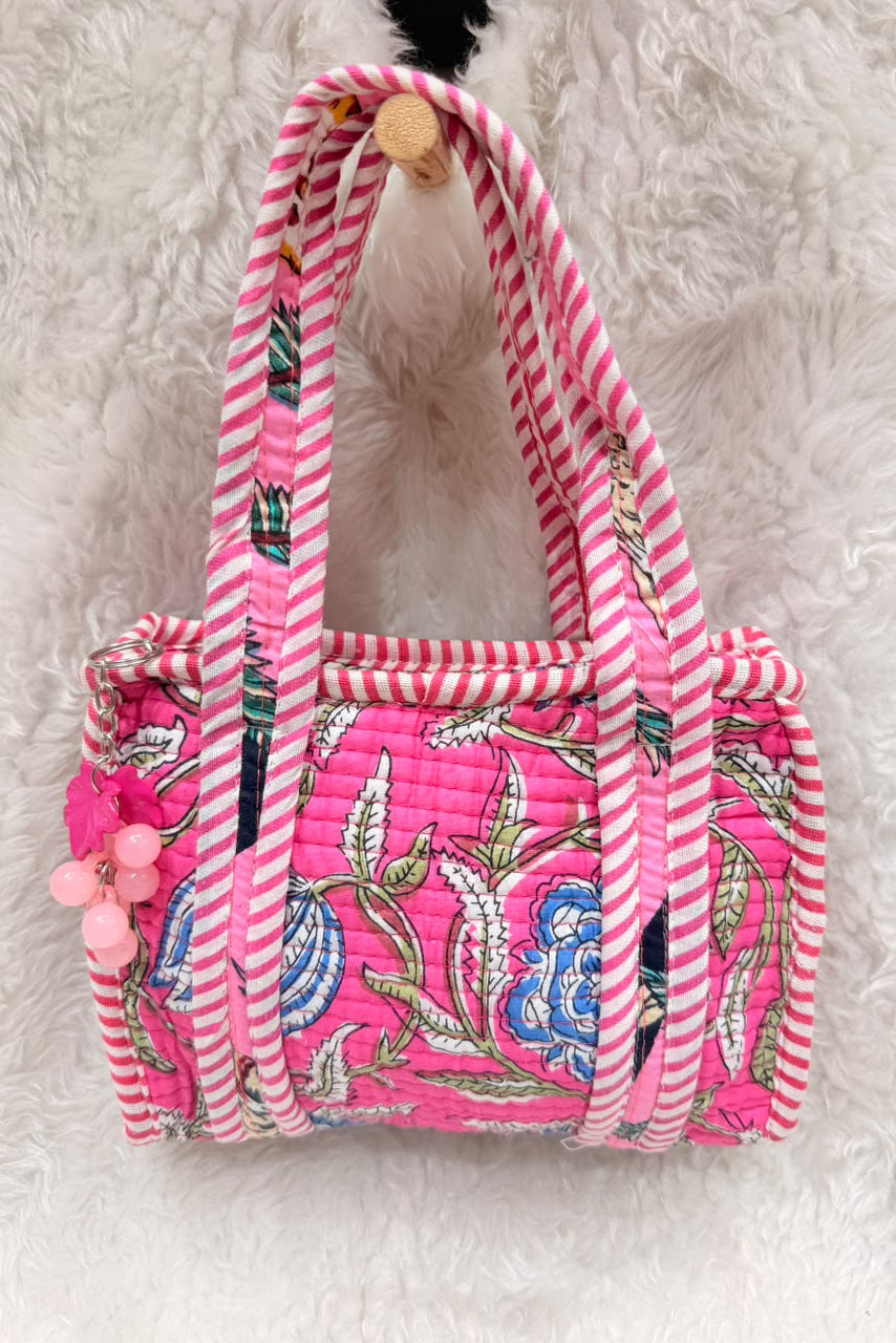 A pink quilted fabric tote bag with white striped handles and a floral print, resting on a white faux fur surface.