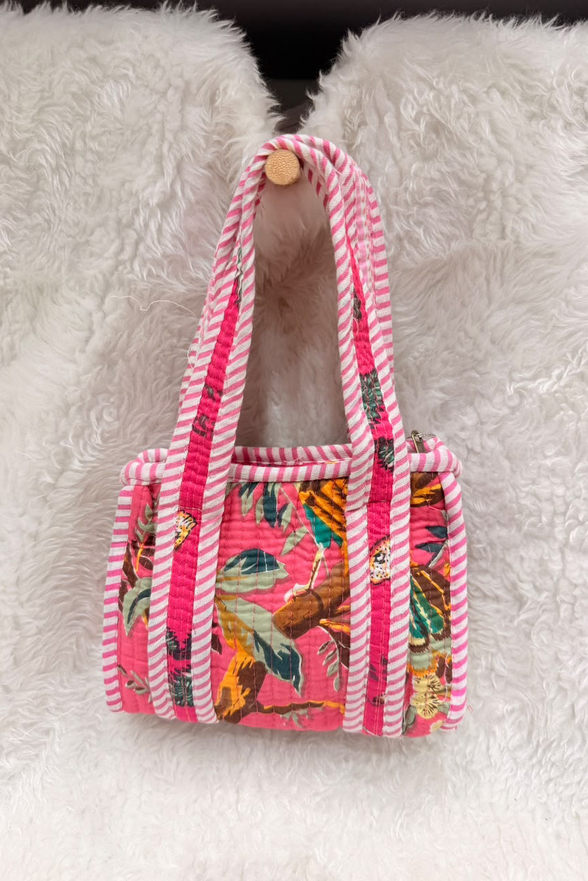 A small tote bag with a pink and white striped rope handle and trim, featuring a colorful tropical bird and floral print on the front, displayed on a white faux fur surface.